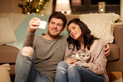 leisure, technology and people concept - happy couple with cat taking selfie by smartphone at home