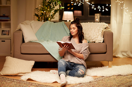 leisure, hygge and people concept - happy young woman reading book at home