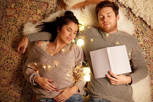 leisure, hygge and people concept - happy couple with book and garland lying on floor at home and sleeping