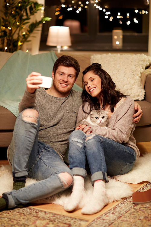 leisure, technology and people concept - happy couple with cat taking selfie by smartphone at home