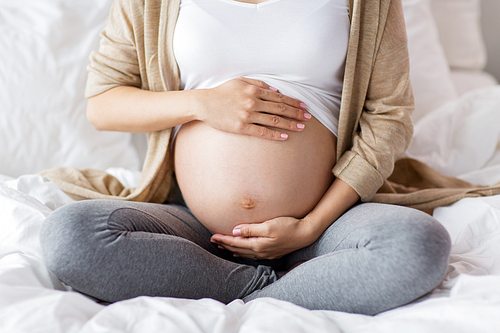 pregnancy, people and maternity concept - pregnant woman sitting in bed at home and touching bare belly