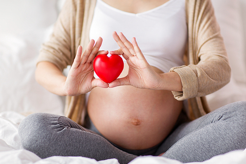 pregnancy, love, people and expectation concept - close up of pregnant woman sitting in bed with red heart