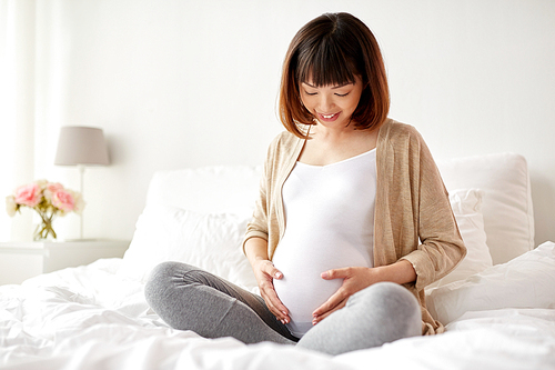pregnancy, people and maternity concept - happy pregnant asian woman sitting in bed at home bedroom