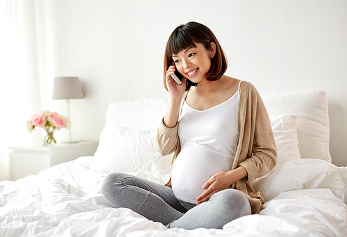 pregnancy, technology and people concept - happy pregnant asian woman calling on smartphone at home