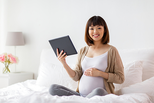 pregnancy, technology, people and expectation concept - happy pregnant asian woman with tablet pc computer in bed at home