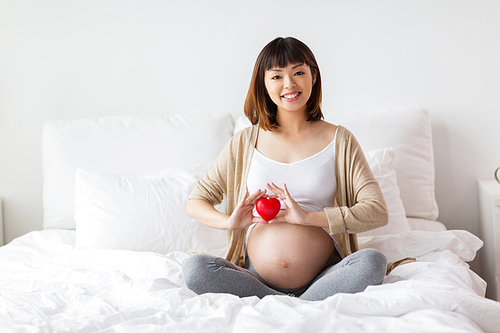 pregnancy, love, people and expectation concept - happy pregnant asian woman sitting in bed with red heart at home