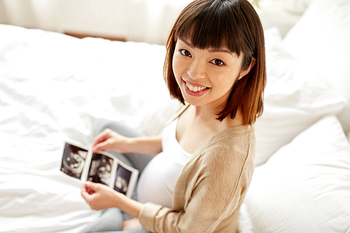 pregnancy and people concept - happy pregnant asian woman with fetal ultrasound image in bed at home