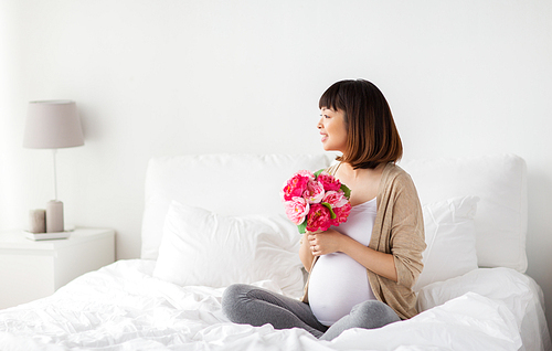 pregnancy, holidays and people concept - happy pregnant asian woman with flowers in bed at home