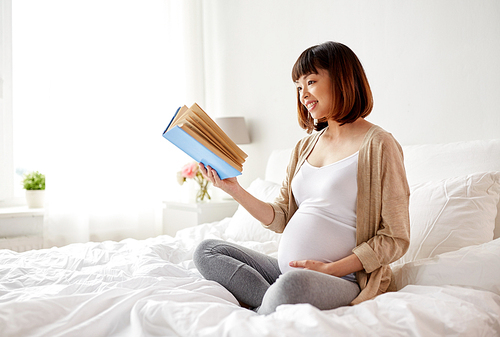 pregnancy and leisure concept - smiling pregnant asian woman reading book in bed at home