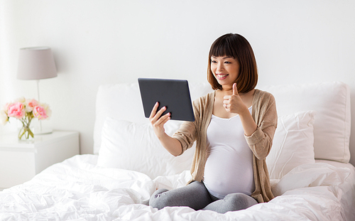 pregnancy, technology and people concept - happy pregnant asian woman with tablet pc computer having video call and showing thumbs up in bed at home