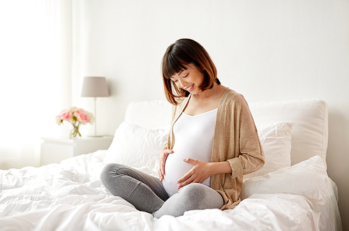 pregnancy, people and maternity concept - happy pregnant asian woman sitting in bed at home bedroom