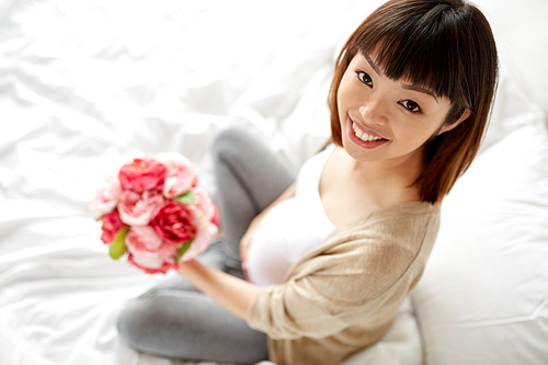pregnancy, holidays and people concept - happy pregnant asian woman with flowers in bed at home