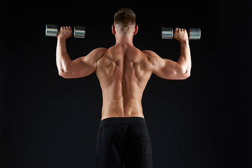 sport, bodybuilding, fitness and people concept - young man with dumbbells flexing muscles over black background from back