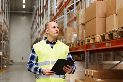 wholesale, logistic, people and export concept - man with clipboard in reflective safety vest at warehouse