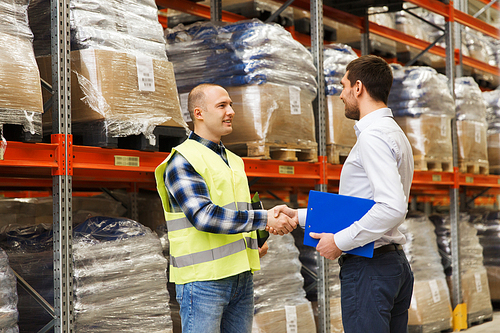 wholesale, logistic, people and export concept - manual worker and businessmen with clipboard shaking hands and making deal at warehouse