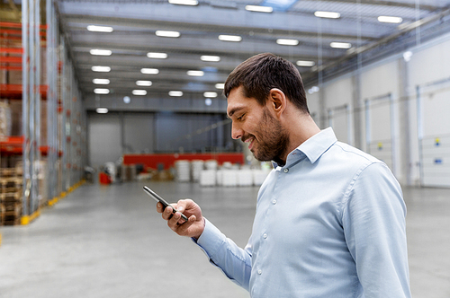 wholesale, logistic business, technology and people concept - businessman with smartphone at warehouse