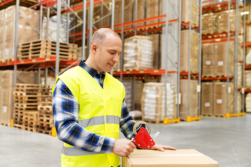 logistic business, shipment and people concept - worker in safety vest packing parcel box with scotch tape at warehouse or  storage