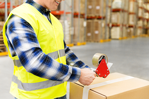 logistic business, shipment and people concept - worker in safety vest packing parcel box with scotch tape at warehouse or mail storage