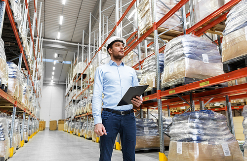 logistic business, shipment and people concept - businessman in helmet with clipboard checking goods at warehouse