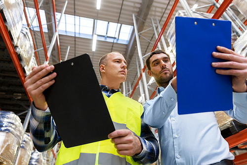 wholesale, logistic business and people concept - manual worker and businessman with clipboards at warehouse