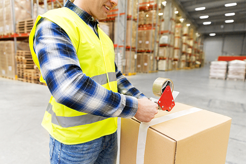 logistic business, shipment and people concept - worker in safety vest packing parcel box with scotch tape at warehouse or mail storage