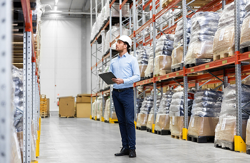 logistic business, shipment and people concept - businessman in helmet with clipboard checking goods at warehouse