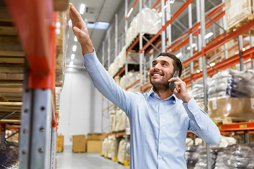 wholesale, logistic business and people concept - smiling businessman calling on smartphone at warehouse