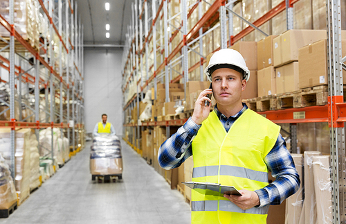 logistic business, technology and shipment concept - businessman calling on smartphone at warehouse