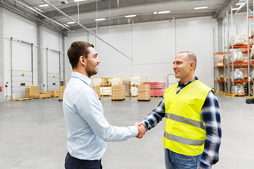 logistic business and cooperation concept - manual worker and businessman with clipboard shaking hands and making deal at warehouse