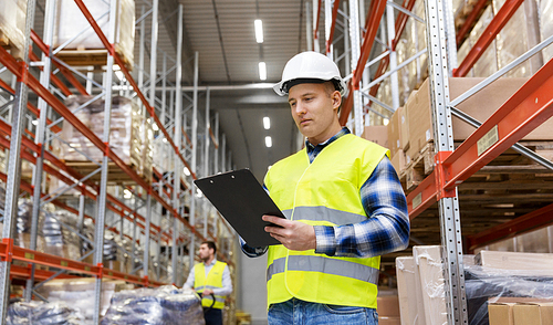 logistic business, shipment and people concept - male worker or supervisor with clipboard in reflective safety vest at warehouse