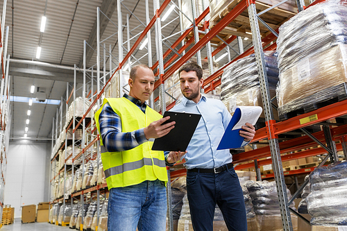 wholesale, logistic business and people concept - manual worker and businessman with clipboards at warehouse