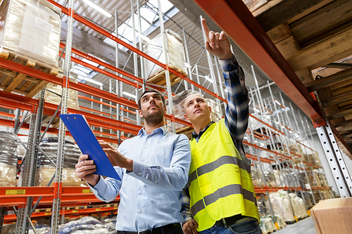 wholesale, logistic business and people concept - manual worker and businessman with clipboards at warehouse