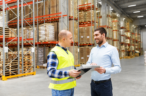 wholesale, logistic business and people concept - warehouse worker and businessman with clipboard and tablet pc computer talking