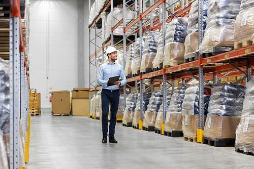 logistic business, shipment and people concept - businessman in helmet with clipboard checking goods at warehouse