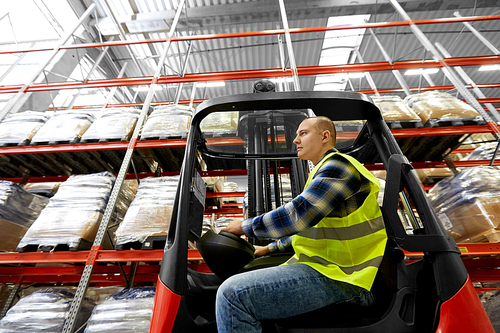 logistic business, shipment and people concept - male worker driving forklift loader at warehouse