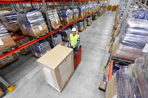 logistic business, shipment and loading concept - loader in helmet operating forklift at warehouse