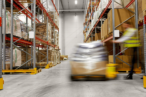 logistic business, shipment and loading concept - motion blurred picture of worker carrying loader with goods at warehouse