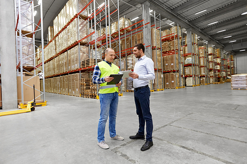 logistic business, shipment and people concept - warehouse worker and businessman with clipboard and tablet pc computer