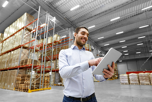 logistic business, shipment and people concept - happy businessman with tablet pc computer checking goods at warehouse