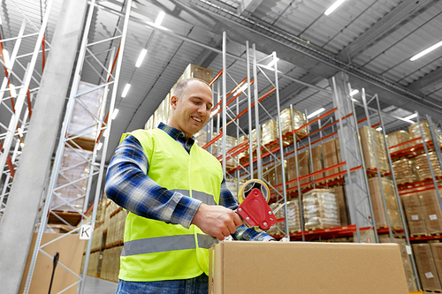 logistic business, shipment and people concept - worker in safety vest packing parcel box with scotch tape at warehouse or mail storage