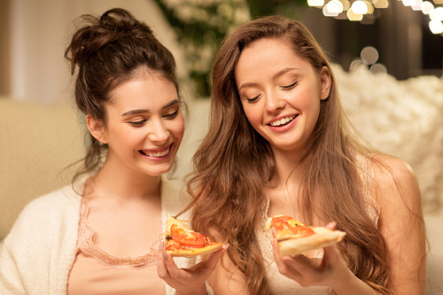 hygge, food and pajama party concept - happy female friends or teenage girls eating pizza at home