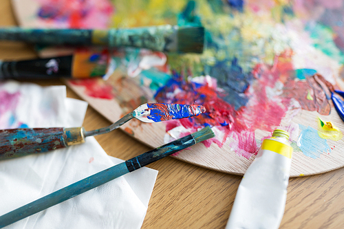 fine art, creativity and artistic tools concept - close up of palette knife or painting spatula, brushes and paint tube