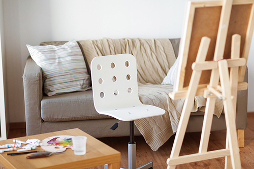 fine art, creativity and artistic tools concept - wooden easel and chair at home room or studio