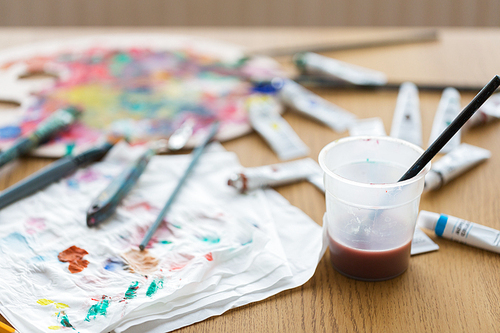 fine art, creativity and artistic tools concept - paintbrush soaking in cup of water and color on paper tissue