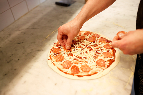 food, culinary, italian cuisine, people and cooking concept - cook hands adding salami slices to pizza at pizzeria