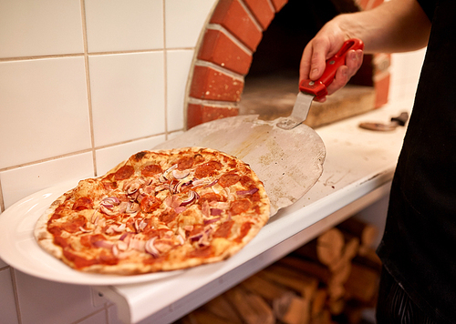 food, italian kitchen, culinary, people and cooking concept - chef placing pizza from peel to plate at pizzeria