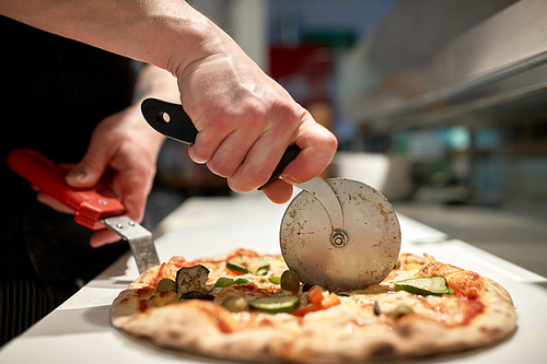 food, italian kitchen and cooking concept - cook with cutter cutting pizza to pieces at pizzeria