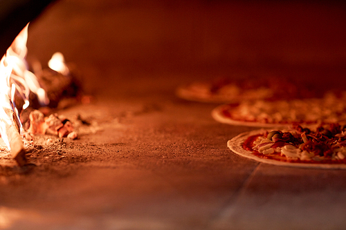 food, italian kitchen and cooking concept - pizza baking in oven at pizzeria