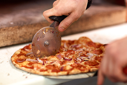 food, italian kitchen and cooking concept - cook hands with cutter cutting pizza to pieces at pizzeria