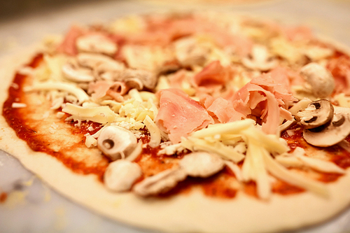 food, culinary, italian cuisine and cooking concept - close up of raw pizza with grated cheese, ham and champignons